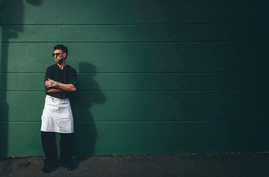 Nathan Sno, founder of Food Story Media, arms folded in a chef's apron against a green wall